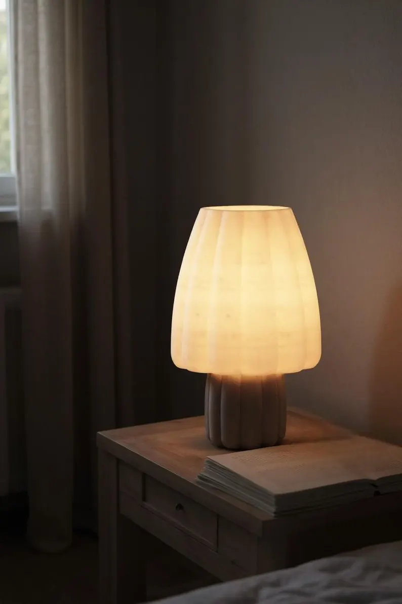 Lámpara Porcini encendida sobre una mesilla de noche